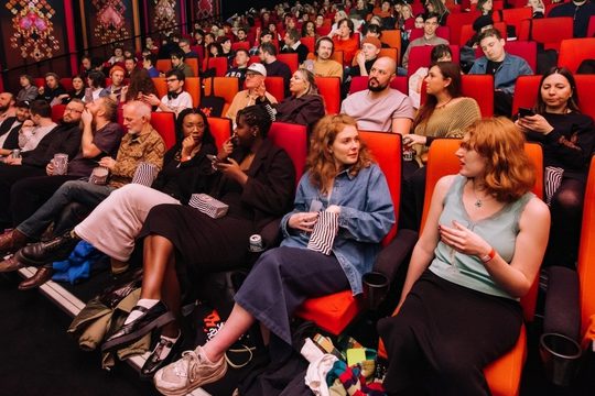 A budy cinema screening, everyone is speaking to each other, with popcorn and drinks in hand.