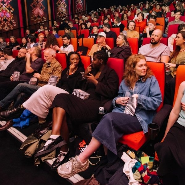 A budy cinema screening, everyone is speaking to each other, with popcorn and drinks in hand.