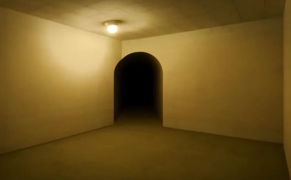 A vacant room with yellow walls. There is a dark tunnel ahead through an arched doorway. The space is dimly lit via a single, small lamp hanging from the ceiling.