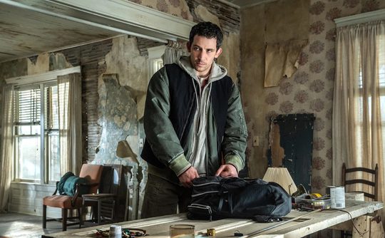 A man (Josh O'Connor) stands centre frame, inside a run down house. He is looking cautiously as he packs a bag rested on a table in front of him.