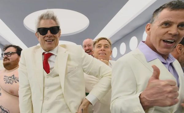 A group of men in white suits in a white room, smiling with thumbs up.