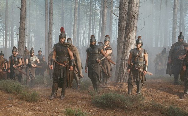 A group of armoured warriors walk towards the camera, through a dense, misty forest.