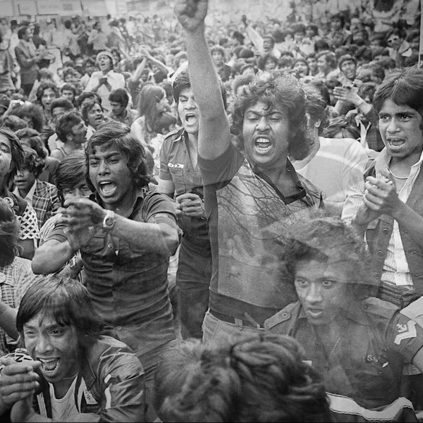 A black and white image of a large, passionate crowd of young people protesting. Some are shouting with raised fists, conveying energy and determination.