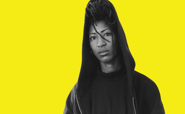 A bright yellow background with an image of a wiman in black and white, from the shoulders upwards. She is wearing a black hoody with her hair up.