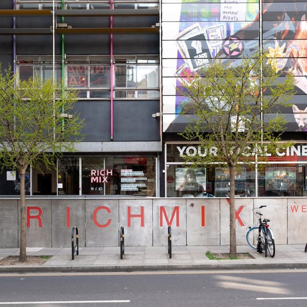 Exterior of Rich Mix cultural center, featuring colourful mural, trees, and bicycles parked by the entrance. The atmosphere is vibrant and inviting.