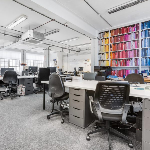 Spacious office with rows of desks, black chairs, and computers. A vibrant wall of rainbow-colored books adds a touch of creativity and energy.