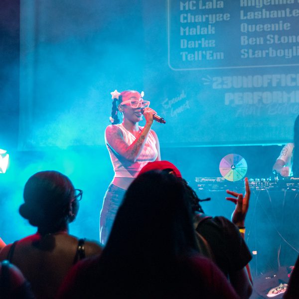 A singer performs confidently on a smoky stage, holding a microphone. A DJ is seen behind them, while a vibrant audience captures the moment.