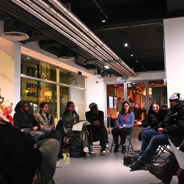 A diverse group of people sit in a circle in a modern, well-lit room, attentively sharing ideas. The setting is casual yet focused and collaborative.